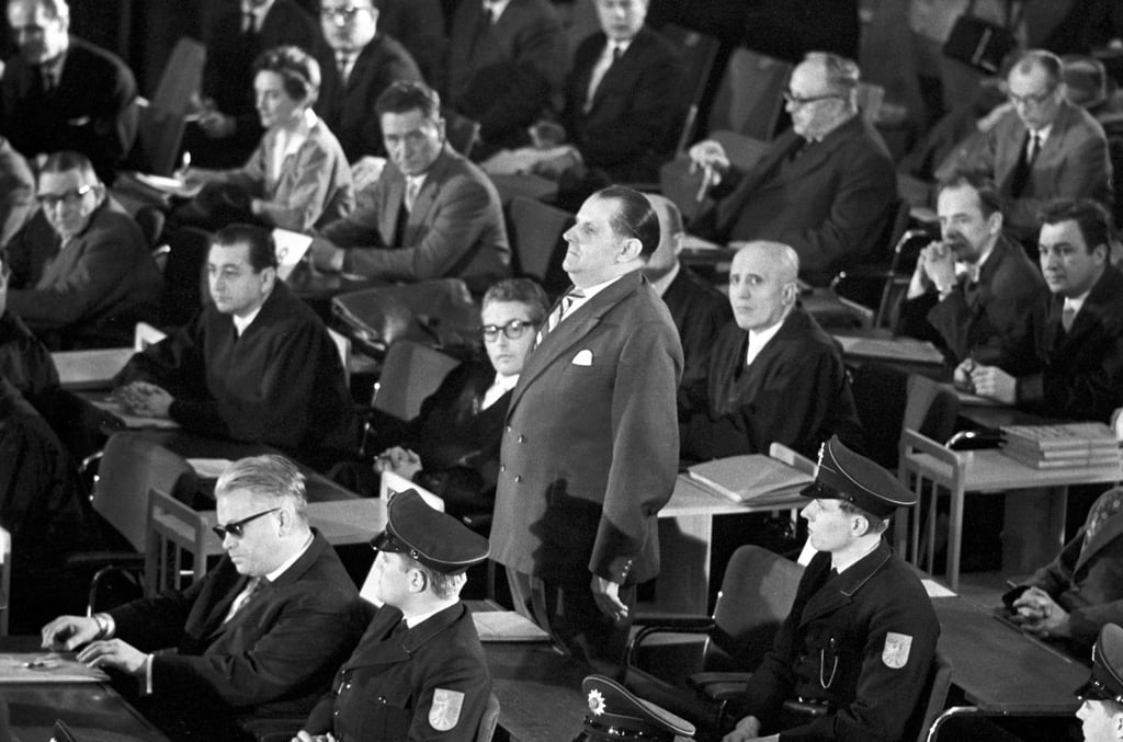 Der erste Auschwitz-Prozess im Plenarsaal der Frankfurter Stadtverordnetenversammlung wird eröffnet. In der ersten Reihe sitzt der Angeklagte Victor Capesius (mit dunkler Brille), hinter ihm steht der Angeklagte Oswald Kaduk. (zu dpa: „Als die Täter von Auschwitz in Frankfurt vor Gericht kamen“)