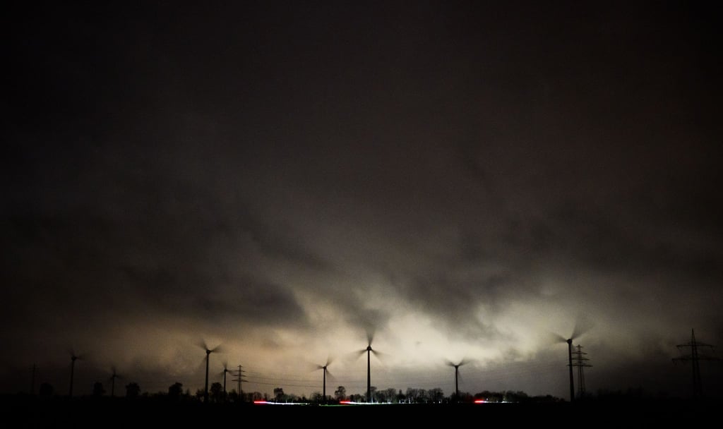 Dunkle Wolken ziehen über sich schnell drehende Windräder.