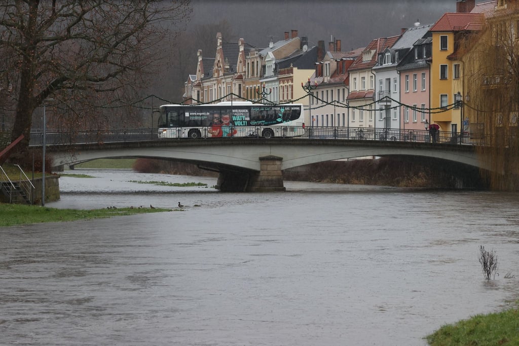 Ein Bus fährt über eine Brücke der Hochwasser führenden Weißen Elster im Zentrum von Greiz.