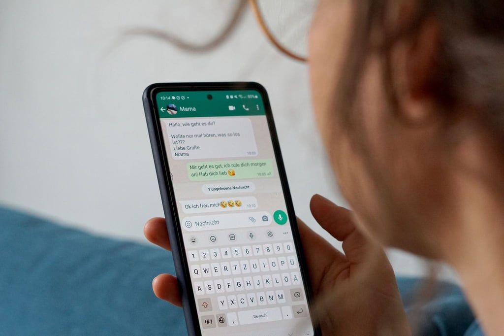 Eine Frau hält ein Smartphone in der Hand, in dem der Messengerdienst WhatsApp geöffnet ist.