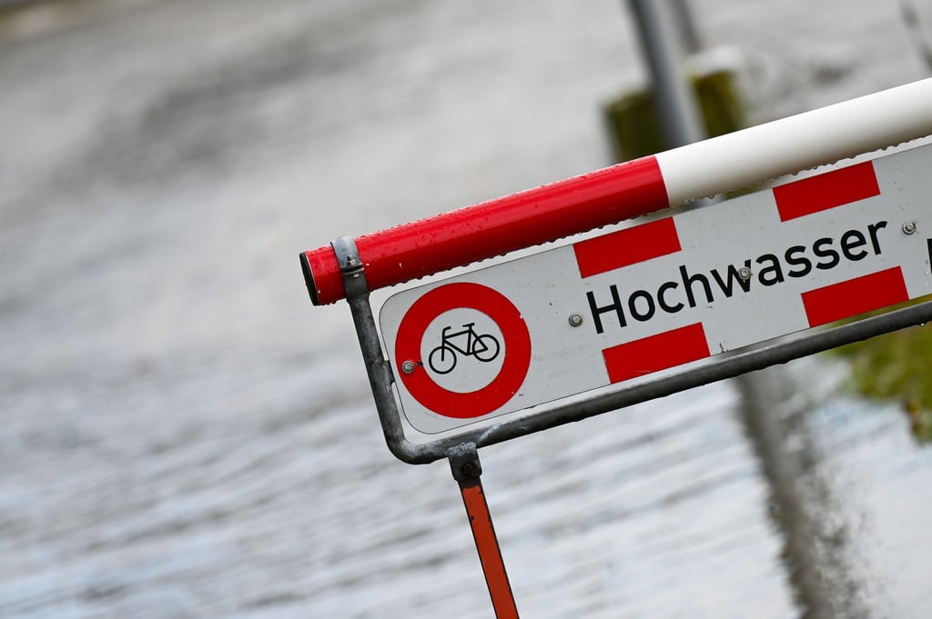 Ein Schild mit der Aufschrift "Hochwasser" steht an einem Fluss.