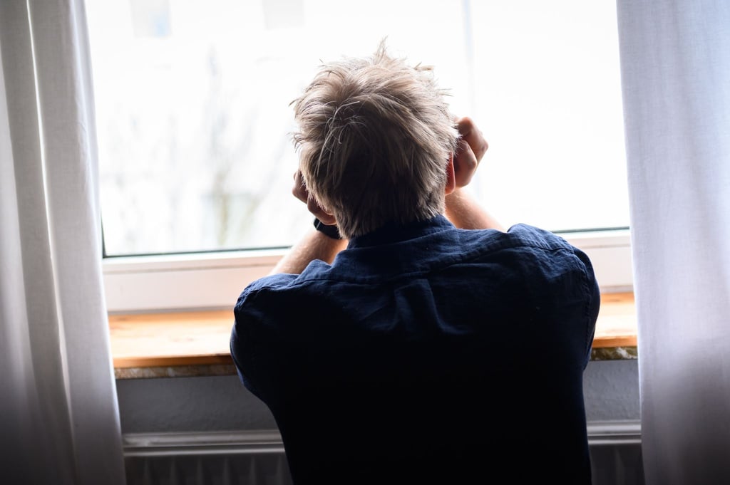 Ein Mann sitzt mit dem Kopf in die Hände gestützt an einem Fenster.