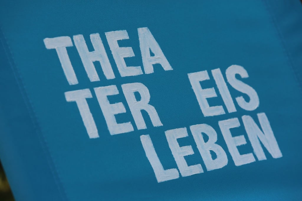 Ein Klappstuhl mit der Aufschrift „Theater Eisleben“ steht auf einer Wiese.
