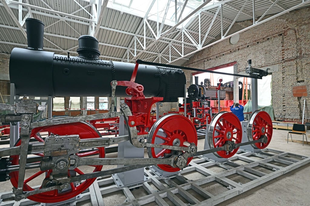 Eine preußische T13 Dampflokomotive wird mit dem Spezialkran in eine Gebäudeöffnung gehoben, wo schon weitere Teile der Lok stehen.