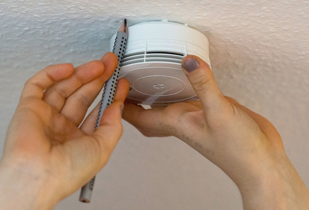 Eine Frau zeichnet mit einem Bleistift an der Decke die Position für einen Rauchmelder an.