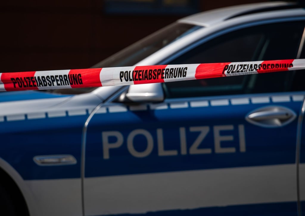 Ein Polizeiauto steht hinter einem Absperrband der Polizei.