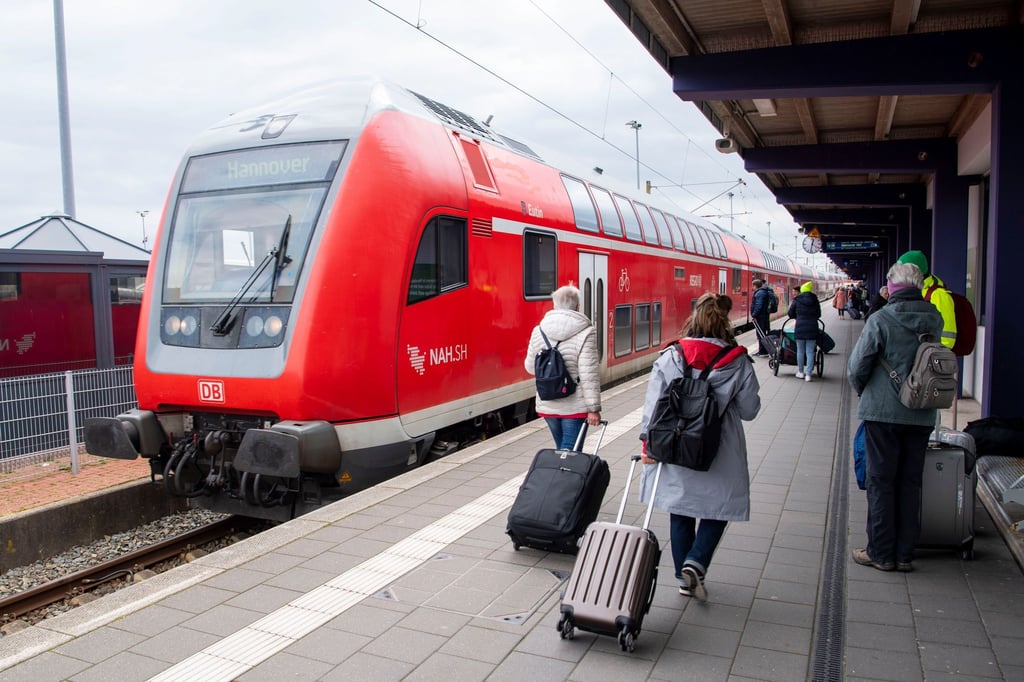 Touristen laufen mit Rollkoffern am Bahnhof Norddeich-Mole entlang.