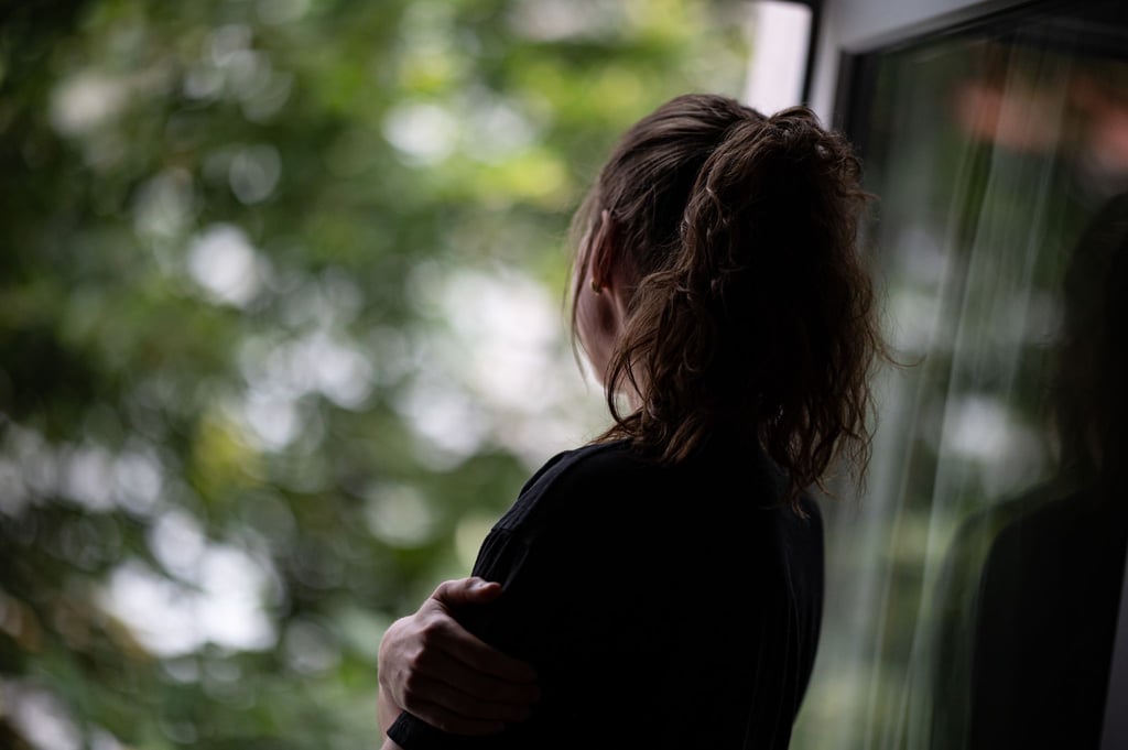 Eine Jugendliche steht gedankenversunken am Fenster. Selbstverletzendes Verhalten kann vorübergehend negative Gefühle verdrängen.