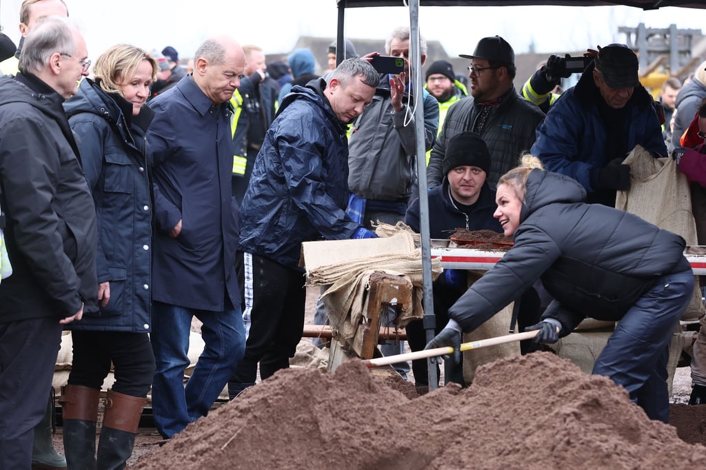 Olaf Scholz (Dritter von links) sieht einer Helferin an der Sandsackbefüllungsstelle in Berga beim Schippen zu. 
