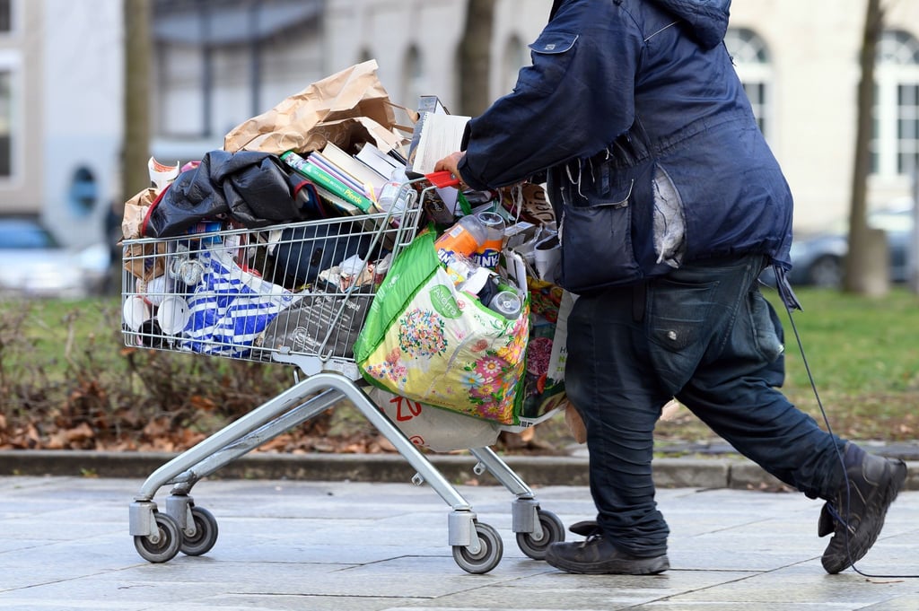 Ein obdachloser Mann schiebt einen Einkaufswagen über eine Fußgängerstraße in Berlin.