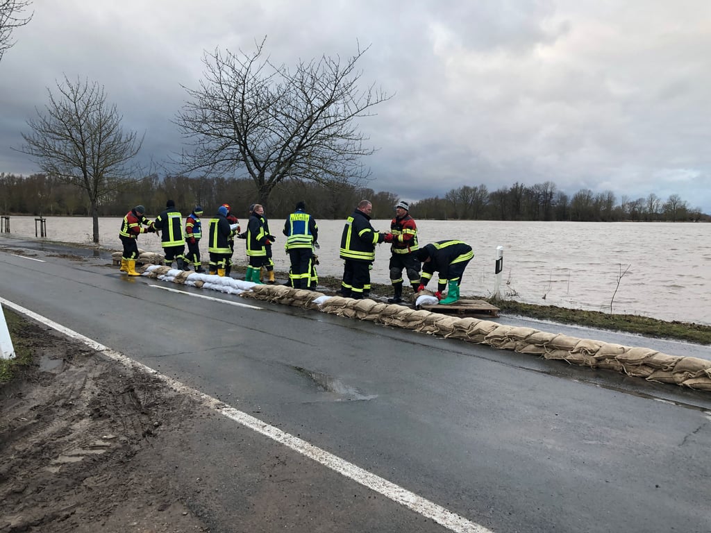 Kampf gegen das Wasser: Feuerwehrleute aus Katharinenrieth und Allstedt versuchen am Vormittag des 4. Janaur 2024, die teilweise überflutete Zufahrtsstraße nach Katharinenrieth mit einem Sandsackdamm halbseitig wieder freizubekommen.