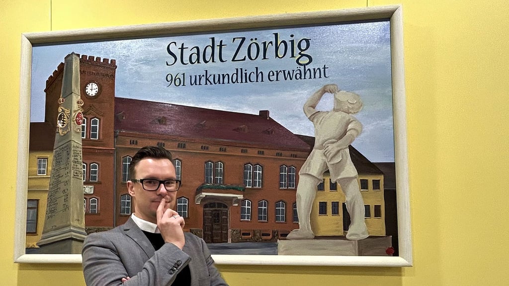 Matthias Egert vor einem Bild mit Rathaus, Saftjunge und Postmeilensäule: Der Zörbiger Bürgermeister äußert sich unter anderem zu Investitionsvorhaben in der Stadt.