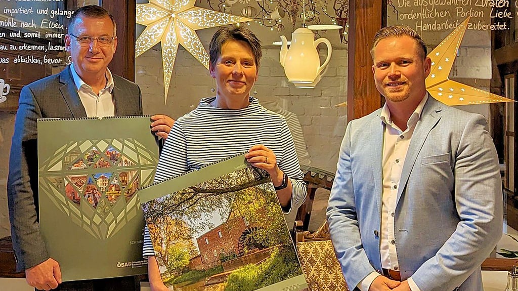 Jan Glöckner und Fred Steinhausen übergeben den Kalender an Evamaria Schmeier, Inhaberin des Cafés in der Wassermühle Elbeu