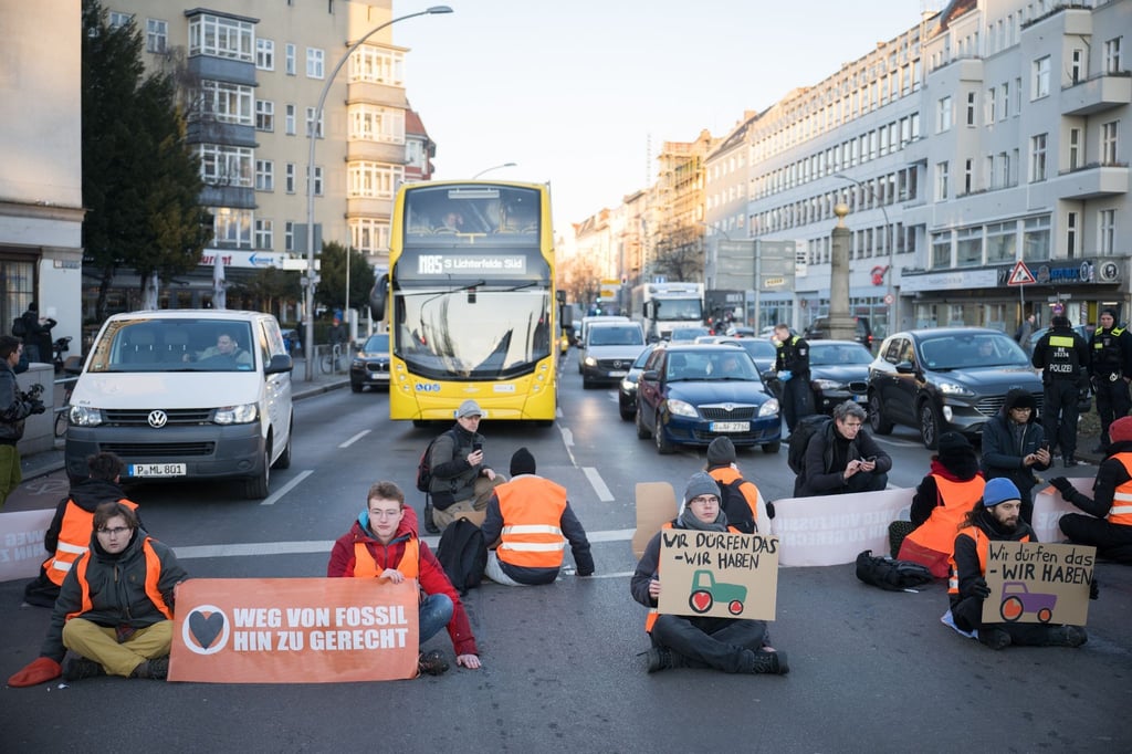 Aktivisten der Klimaschutzgruppe Letzte Generation sitzen bei einer Straßenblockade auf der Straße.