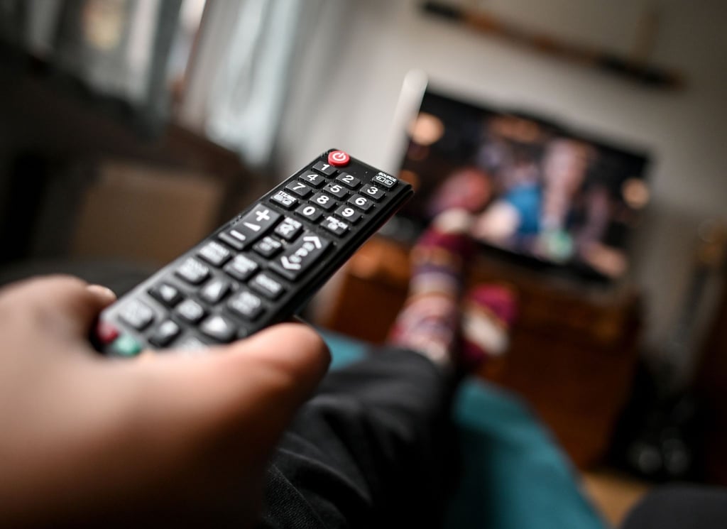 Ein junger Mann sitzt mit einer Fernbedienung vor dem Fernseher.