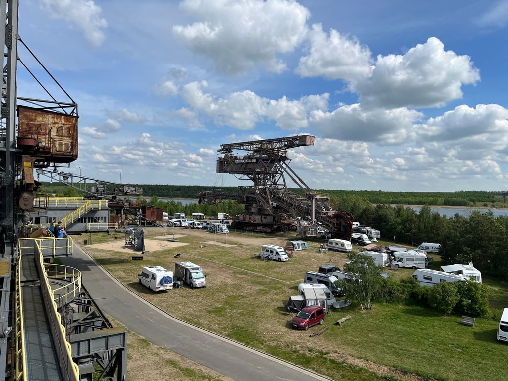 Zahlreiche Wohnwagen und Wohnmobile stehen unter einem Schaufelradbagger in Ferropolis.