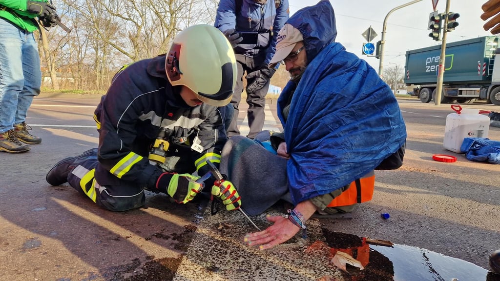 'Feuerwehr im Einsatz gegen Straßenblockade: Der letzte Klimakleber wird von der Paracelsusstraße in Halle gemeißelt.