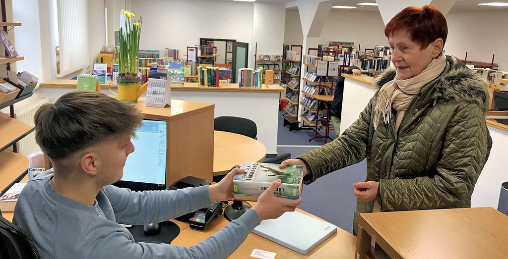 Student Max Sierig ist einer von zwei Minijobbern, die seit Dezember in der Barleber Bibliothek arbeiten. Leserin Sonja Aßmann freut sich, dass die Einrichtung nach monatelanger Schließung wieder geöffnet hat.