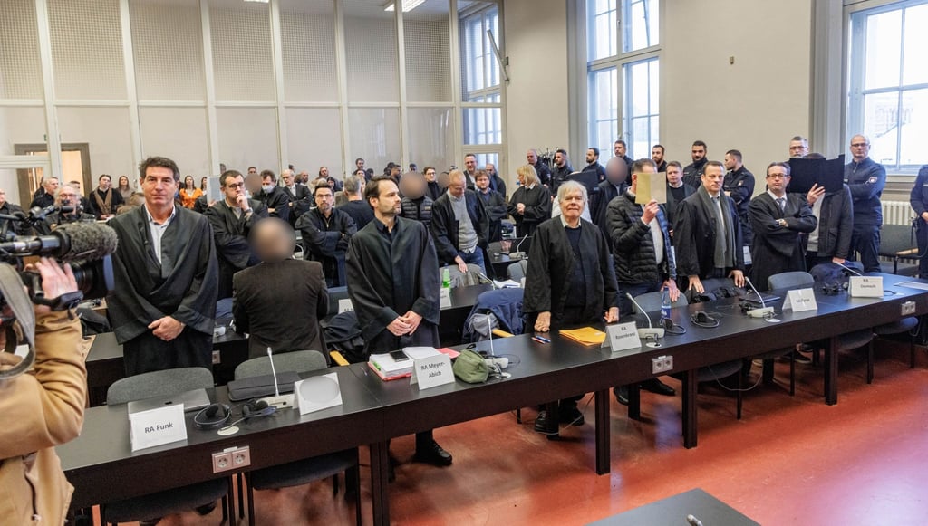 Die Angeklagten und ihre Verteidiger stehen vor der Urteilsverkündung im Gerichtssaal.