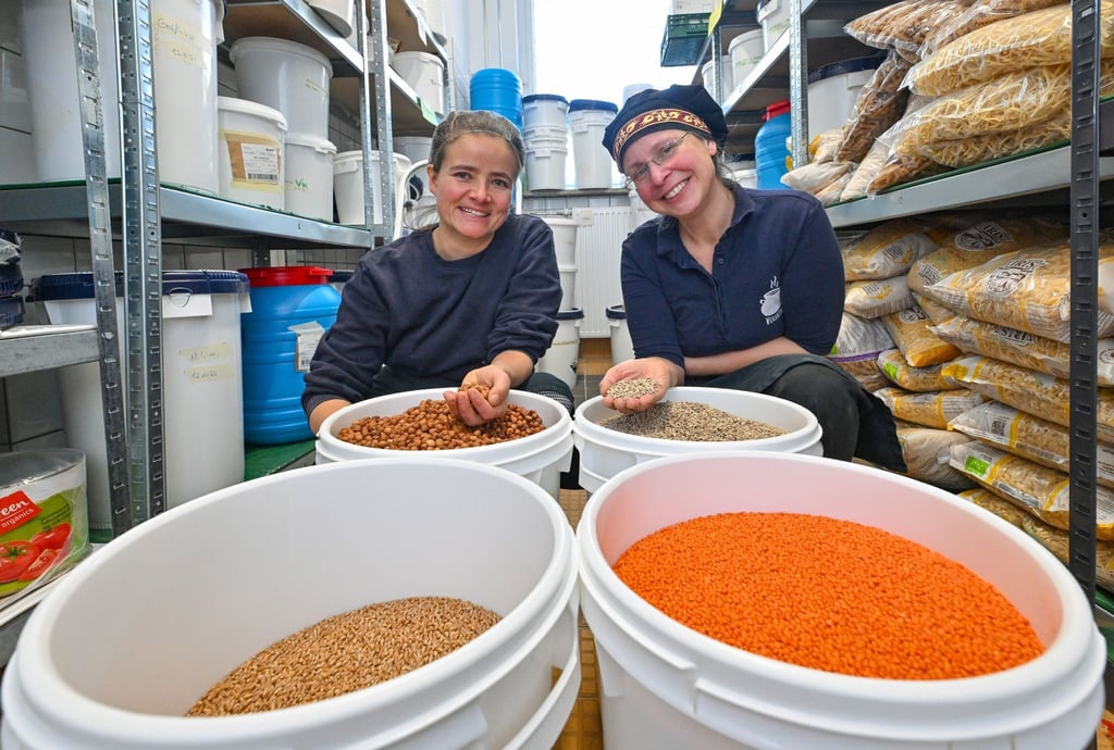 Franziska Ernst (l) und Annette Schmidt, beide leiten die Wukantina, sind im Lager mit Behältern voller Getreide, Linsen und Nüssen zu sehen.