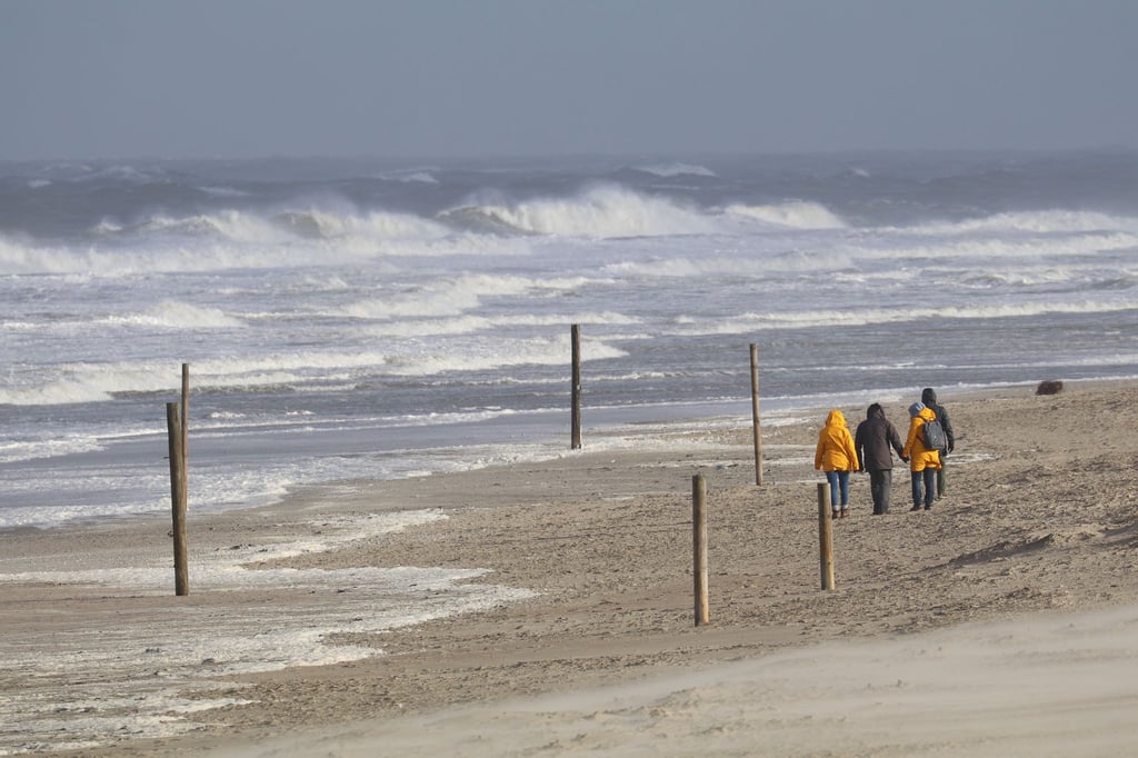 Bei stürmischem Wetter und Wellen gehen Spaziergänger am Strand entlang.