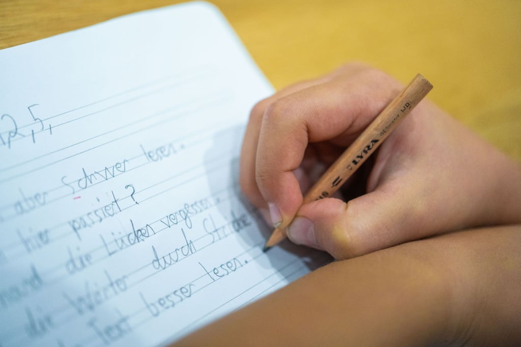 Ein Grundschüler sitzt an einem Tisch und schreibt mit einem Bleistift in sein Heft.