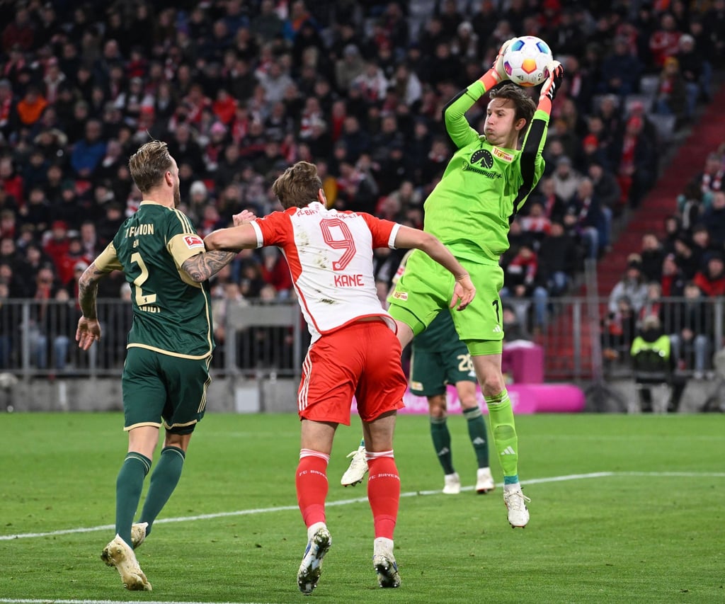 Torhüter Frederik Ronnow von Berlin (r) hält den Ball in der Luft fest, während Kevin Vogt von Berlin (l) und Harry Kane von München (M) in Aktion sind.