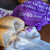 Eine zerknüllte Brottüte der Bäckereikette Lila Bäcker liegt neben einem Brötchen. Die Backkette Lila Bäcker ist insolvent.