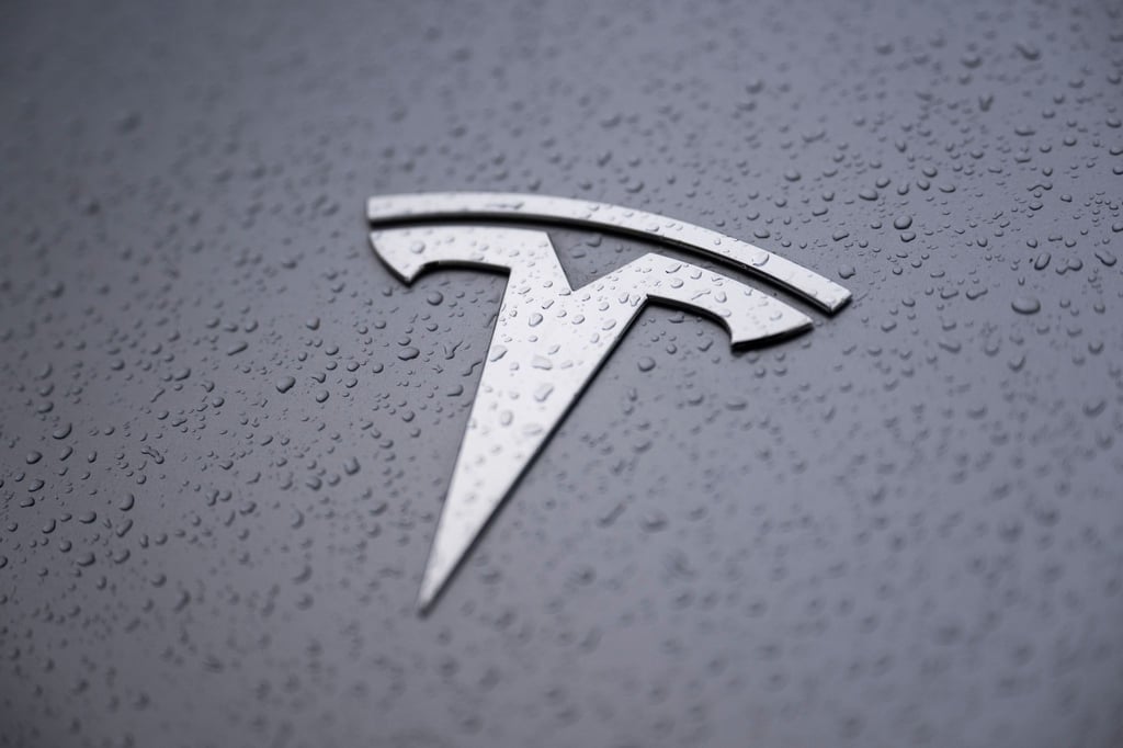 Ein verregnetes Auto mit dem Tesla Logo auf einem Parkplatz.