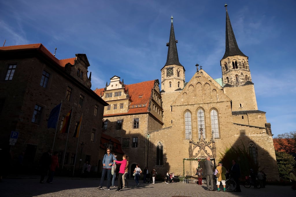 Besucher gehen vor dem Merseburger Dom nach der Weihe der neuen Glocke über den Domplatz.