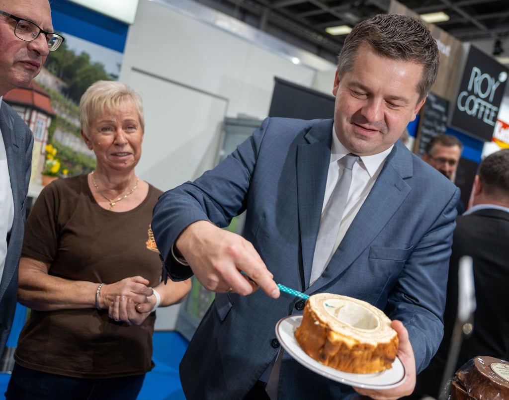 Sven Schulze (CDU) schneidet Baumkuchen am Stand der Firma Baumkuchen Hennig beim Rungang auf der Grünen Woche.