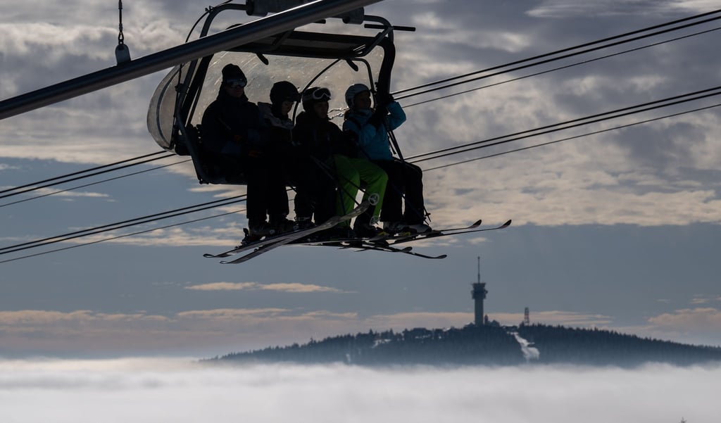 Wintersportler sitzen mit ihren Ski über den Wolken vor der Kulisse des 1243 Meter hohen Keilbergs in einem Lift und fahren auf den Gipfel des Fichtelbergs.