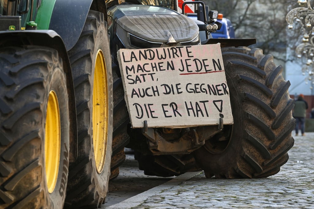 Ein Protestplakat mit der Aufschrift „Landwirte mache jeden satt, auch die Gegner die er hat!“ ist an einem Traktor befestigt.