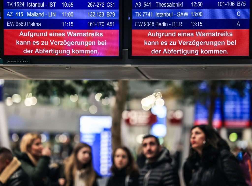 Auf einer Anzeigetafel steht der Schriftzug „Aufgrund eines Warnstreiks kann es zu Verzögerungen bei der Abfertigung kommen“.