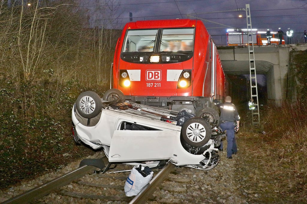 Das Unfallauto liegt unterhalb einer Brücke in Stuttgart vor einer Lokomotive auf den Gleisen.