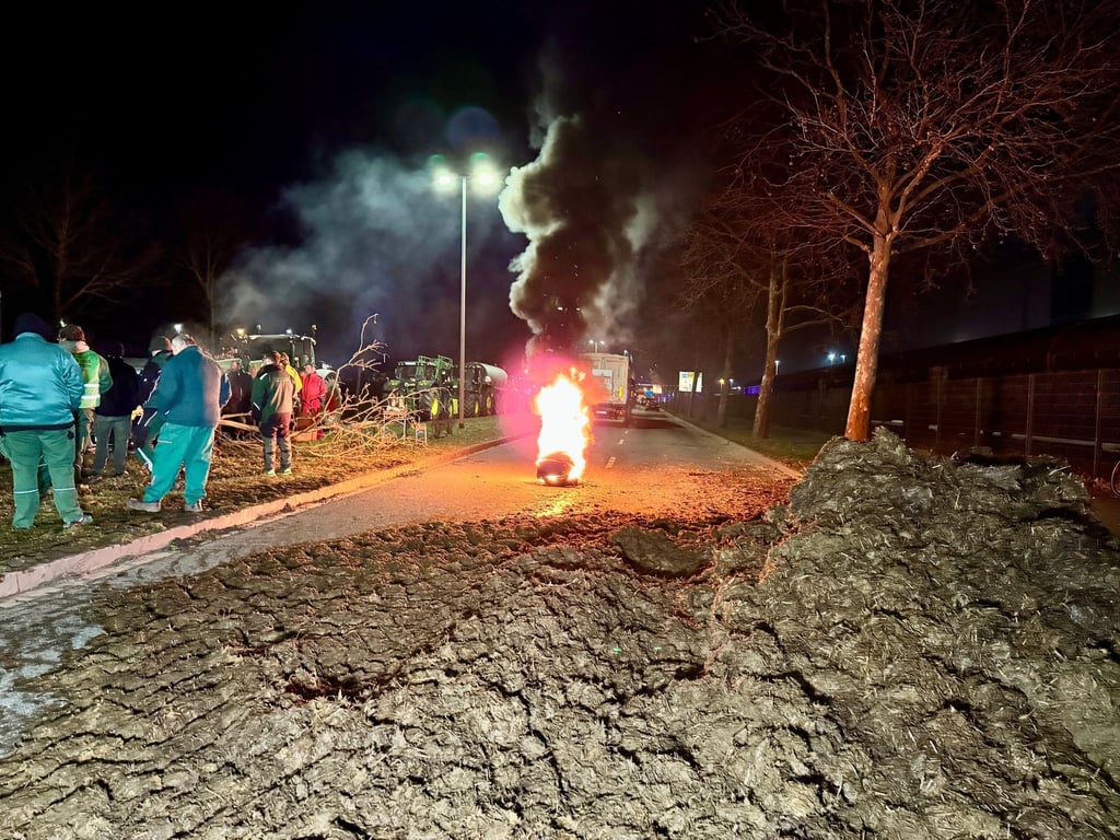 Landwirte blockieren mit Mist und brennenden Reifen eine Straße bei Magdeburg.