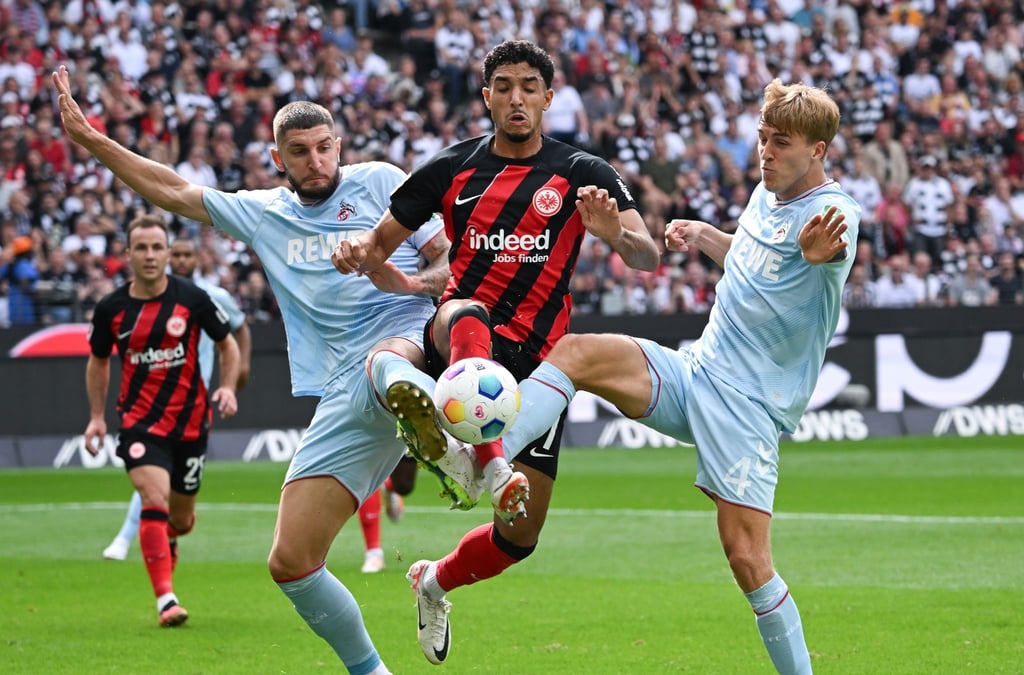 Frankfurts Omar Marmoush (M) im Zweikampf mit Jeff Chabot (l) und Timo Hübers vom 1. FC Köln.