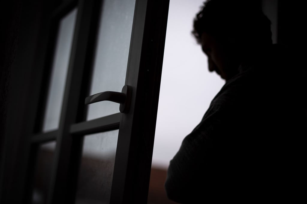 Ein Mann steht am offenen Fenster seiner Wohnung.