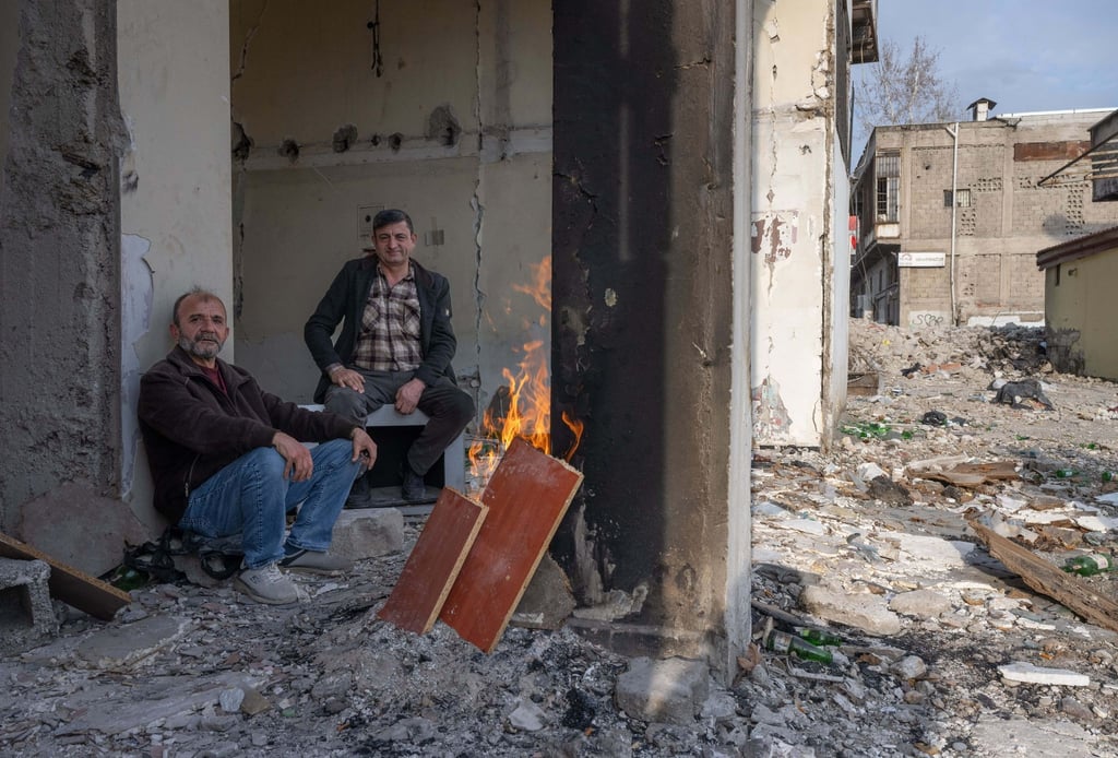 Zwei Männer wärmen sich in den Trümmern eines zerstörten Hauses in Kahramanmaras an einem Feuer. Im Zentrum der Stadt waren bei dem Beben vor einem Jahr unzählige Häuser zerstört oder beschädigt worden.