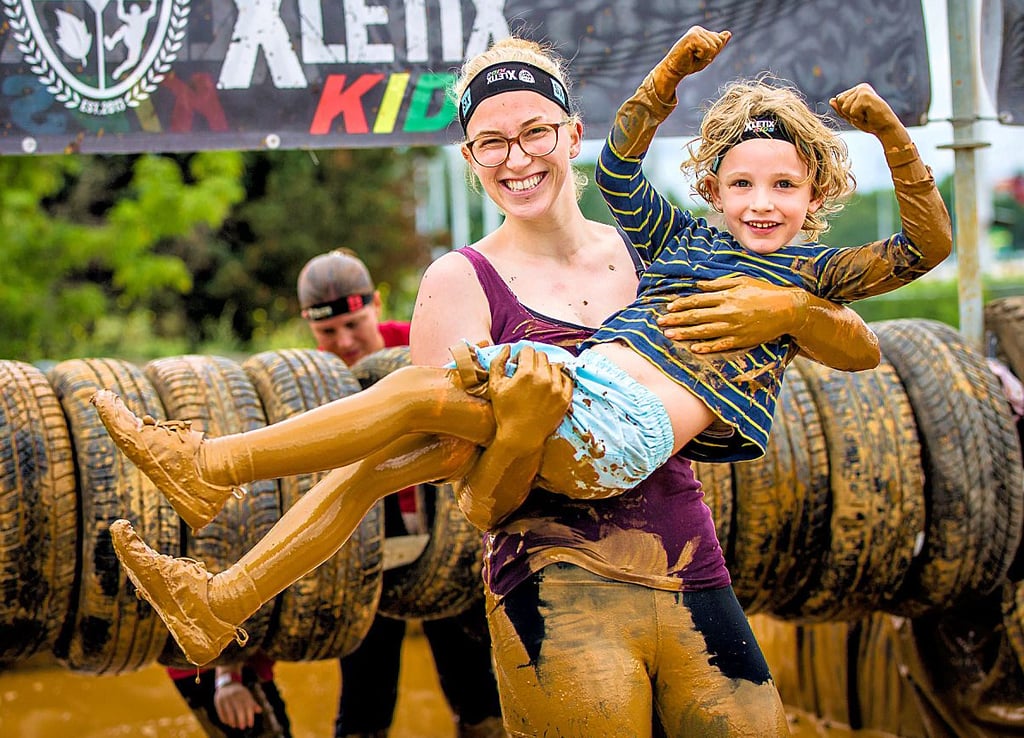 Ein Eindruck von „Xletix Kids“ aus Berlin. Das Event richtet sich an die ganze Familie. Im Hintergrund ist ein Reifen-Hindernis zu sehen.