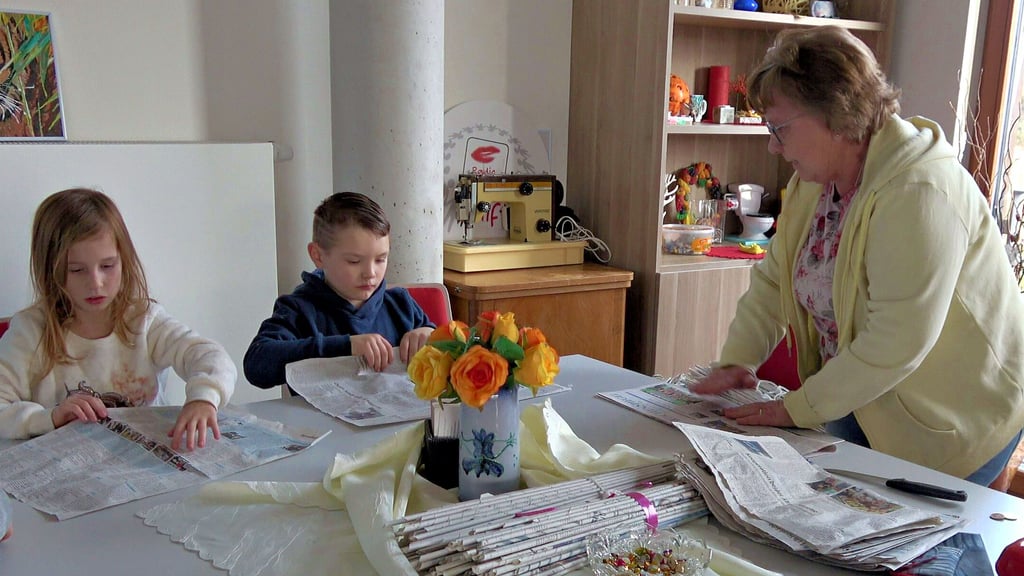Kinder basteln mit Petra Güldenpfennig einen Kranz aus Zeitungspapier im Jugendklub in Kamern. Als erstes werden Blätter zu Röhren gedreht.