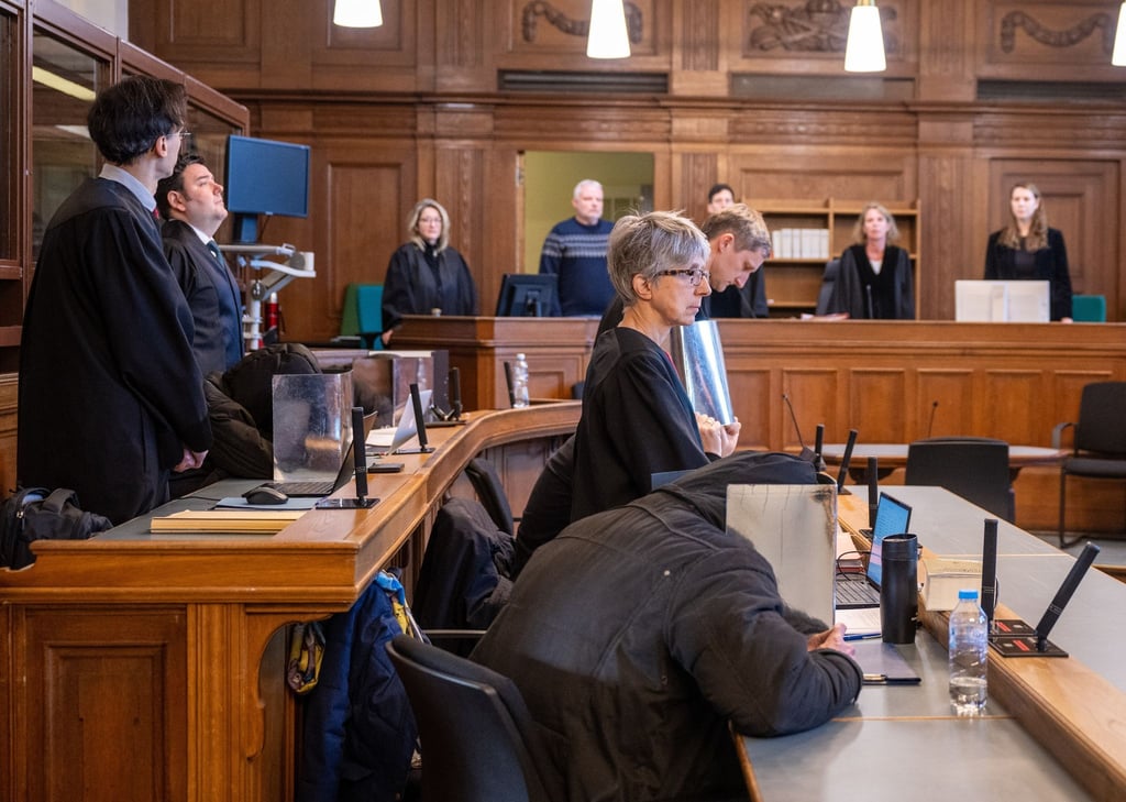 Vier Angeklagte sitzen vor Beginn der Verhandlung im Gerichtssaal im Kriminalgericht Moabit in Begleitung ihrer Anwälte und verdecken dabei ihre Gesichter mit Pappe.