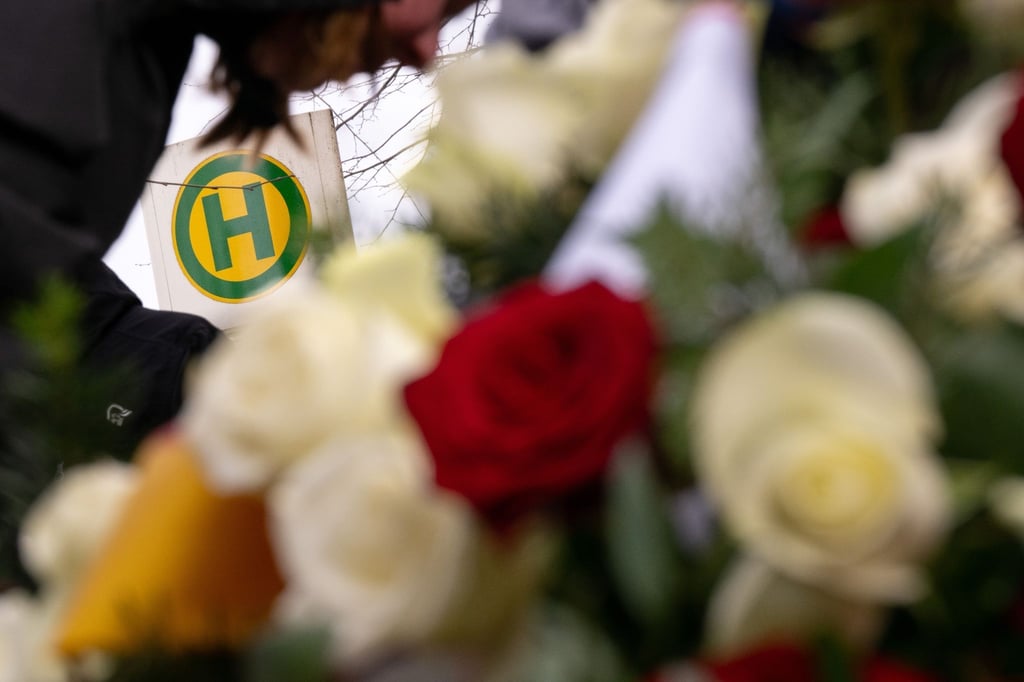 Blumen liegen während einer Gedenkveranstaltung an dem Gedenkstein vor dem Schild der Bushaltestelle.