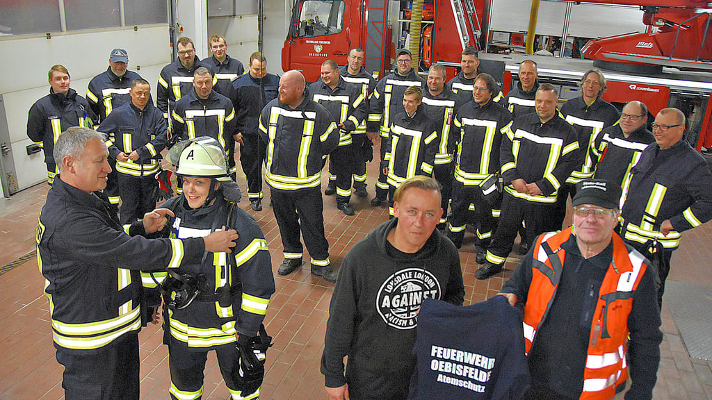 Oebisfeldes Ortswehrleiter Frank Hartwig (l.) hift Feuerwehrfrau Lilla Kiraly beim Anlegen des Atemschutzgerätes. Michael Frank (r.) überreicht 15 Trainingsanzüge für die Atemschutzträger. Hauptfeuerwehrmann Christian Löbe probiert seine Wechseljacke gleich an.