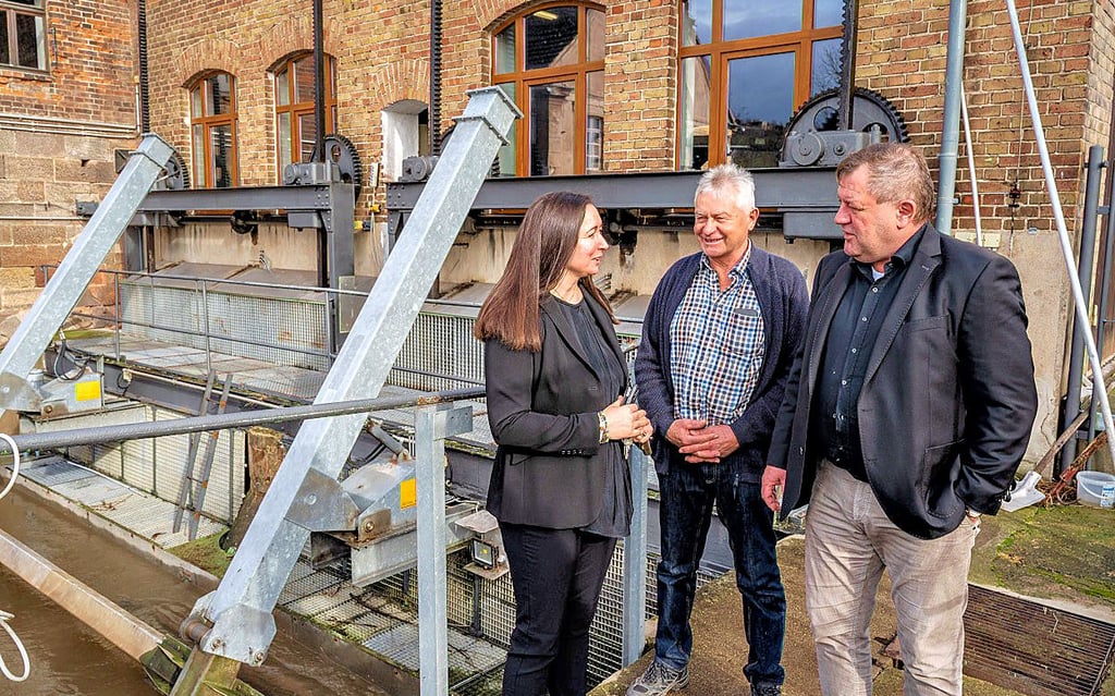 Jana Schäfer von der Mühle Zeddenbach im Gespräch mit Sven Richter (r.), Geschäftsführer der Ingenieurgesellschaft für Wasserkraftanlagen, und Gerhard Rauch, Vorstandsmitglied des Wasserkraftverbandes Mitteldeutschland. Im Hintergrund die Mühle und die Wasserkraft-Anlage aus dem Jahr 1911.