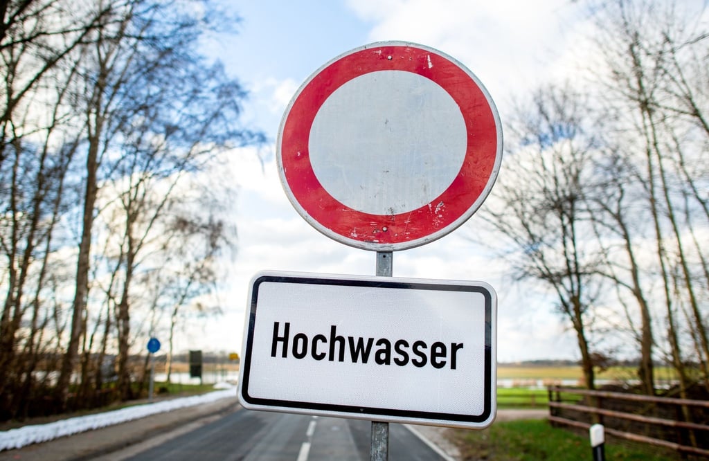 Ein Schild mit der Aufschrift "Hochwasser" steht vor einer gesperrten Straße.