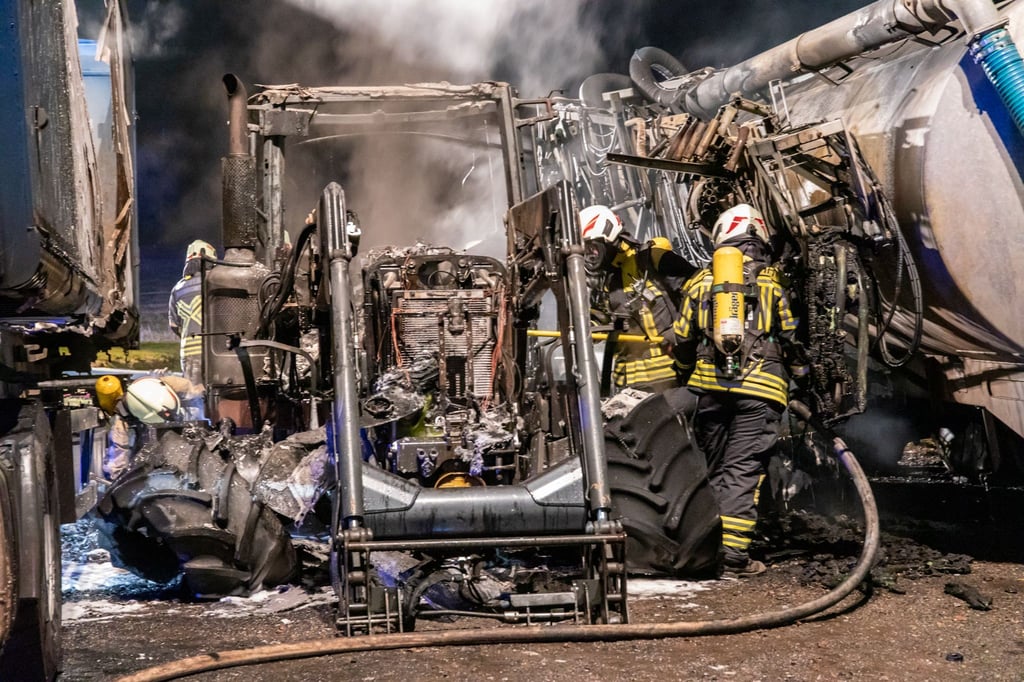 Feuerwehrleute stehen zwischen verbrannten landwirtschaftlichen Geräten.