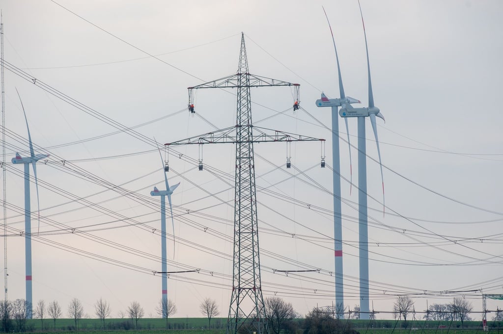 Techniker hängen in Sitzen am Mast einer Stromtrasse und arbeiten an den Leitungen.