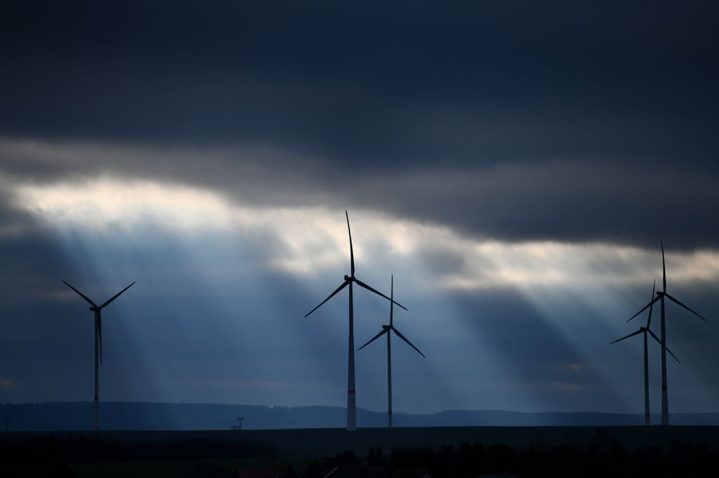 Die Sonne bricht hinter Windrädern durch eine Wolkendecke über Großwechsungen.
