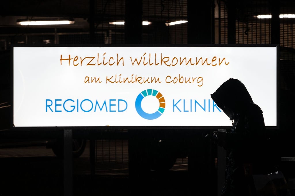 Eine Frau geht mit gesenktem Kopf am Eingangsschild des Regiomed-Klinikums in Coburg vorbei.